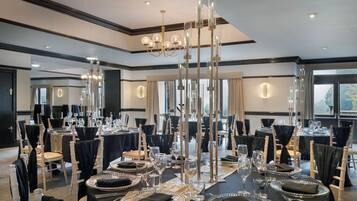 Un salón de banquetes con mesas redondas dispuestas para comer, candelabros altos y un diseño de interiores moderno.