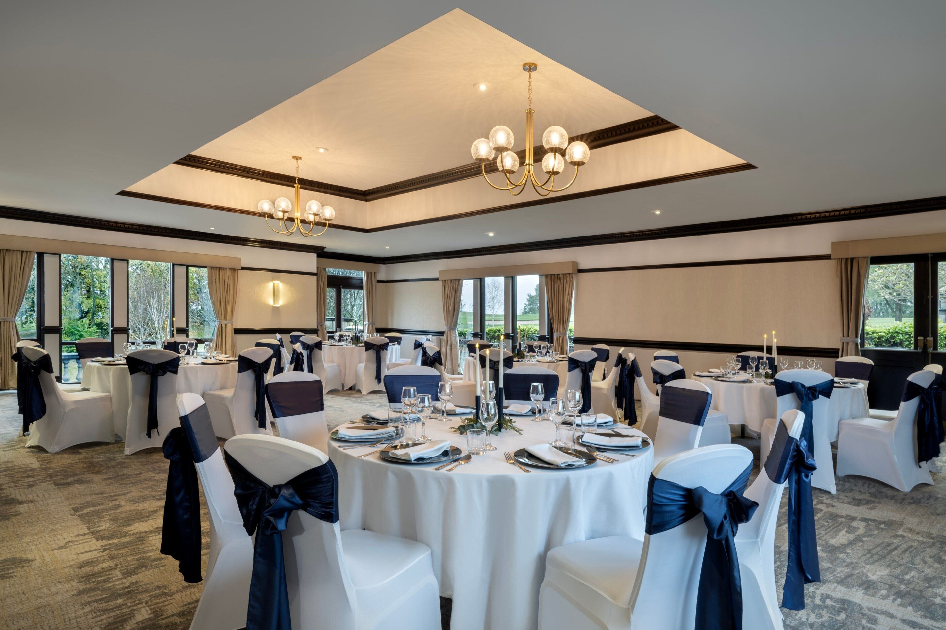 A banquet hall with round tables, white chairs, and chandeliers.