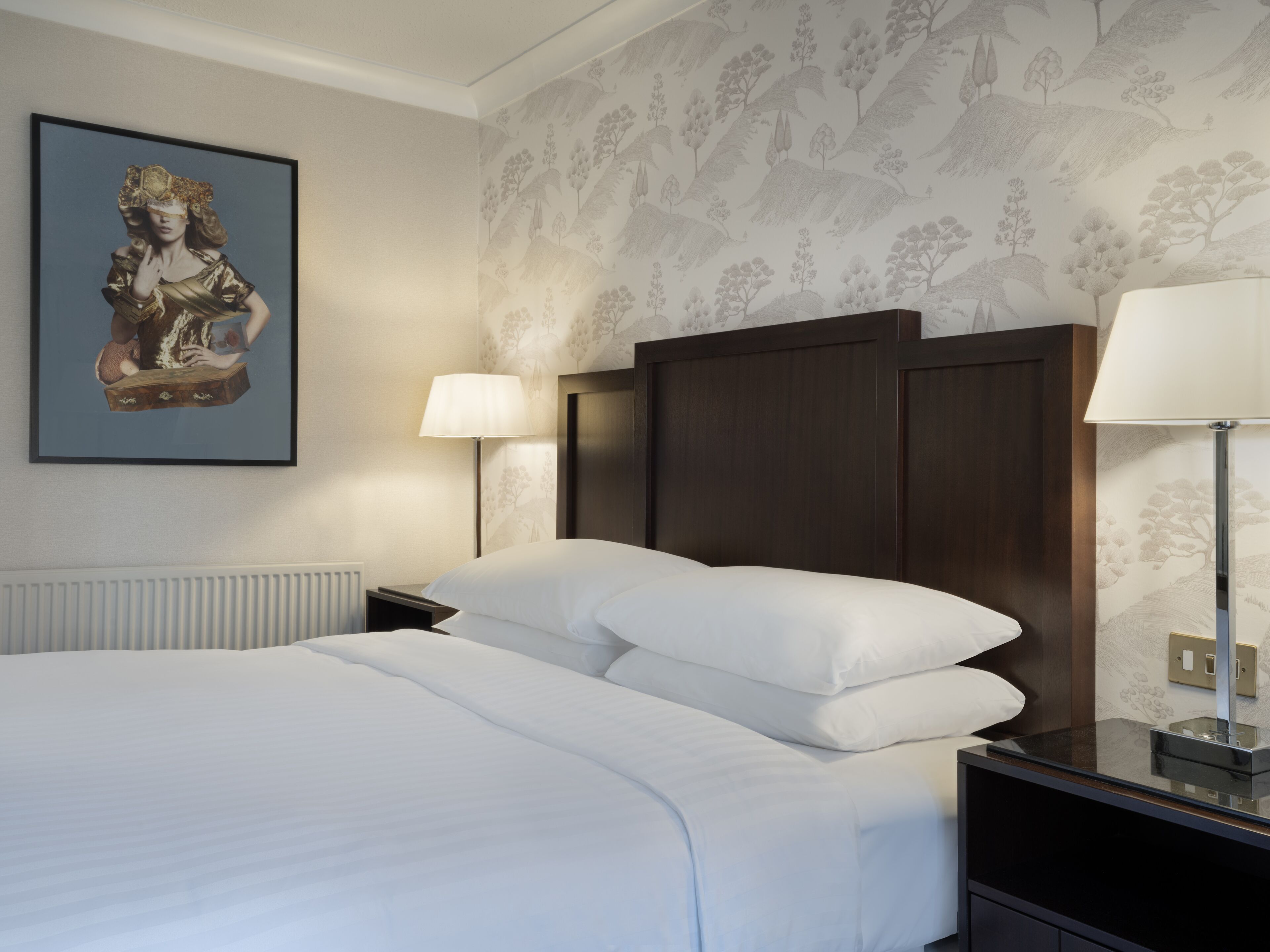 Ein ordentlich gemachtes Bett mit weißen Laken, einem dunklen Holzkopfende und einer Wandlampe.
