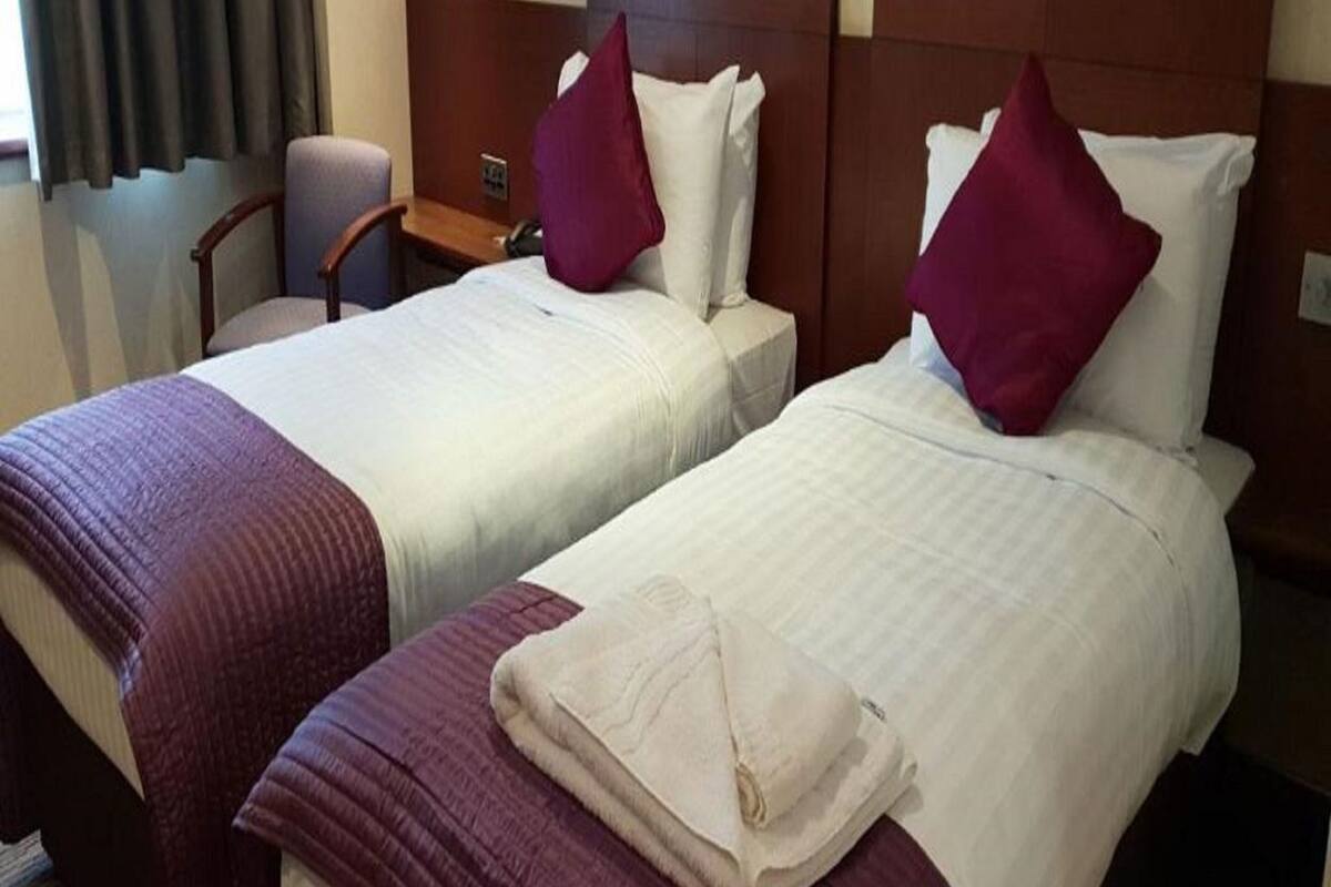 Dos camas de hotel juntas con cabeceros, una silla y un escritorio con teléfono.