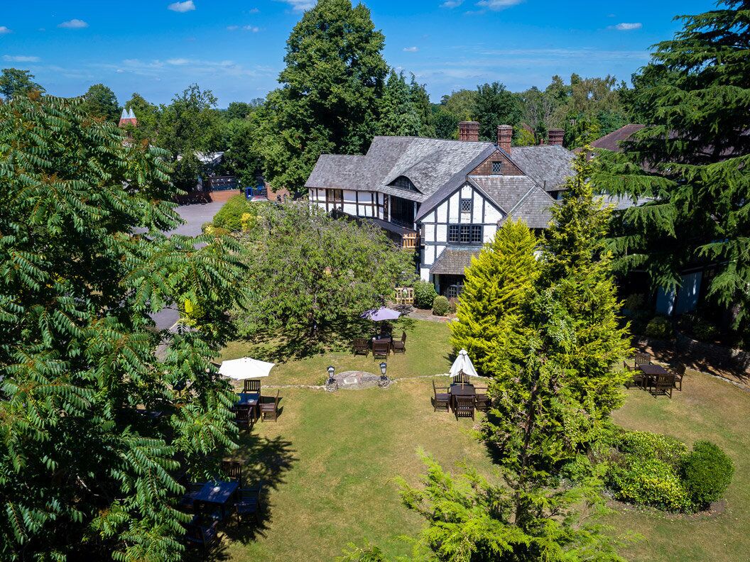 Un bâtiment de style Tudor traditionnel, doté d’un jardin bien entretenu, d’un espace extérieur aménagé pour s’asseoir et offrant une vue dégagée sur les arbres environnants.
