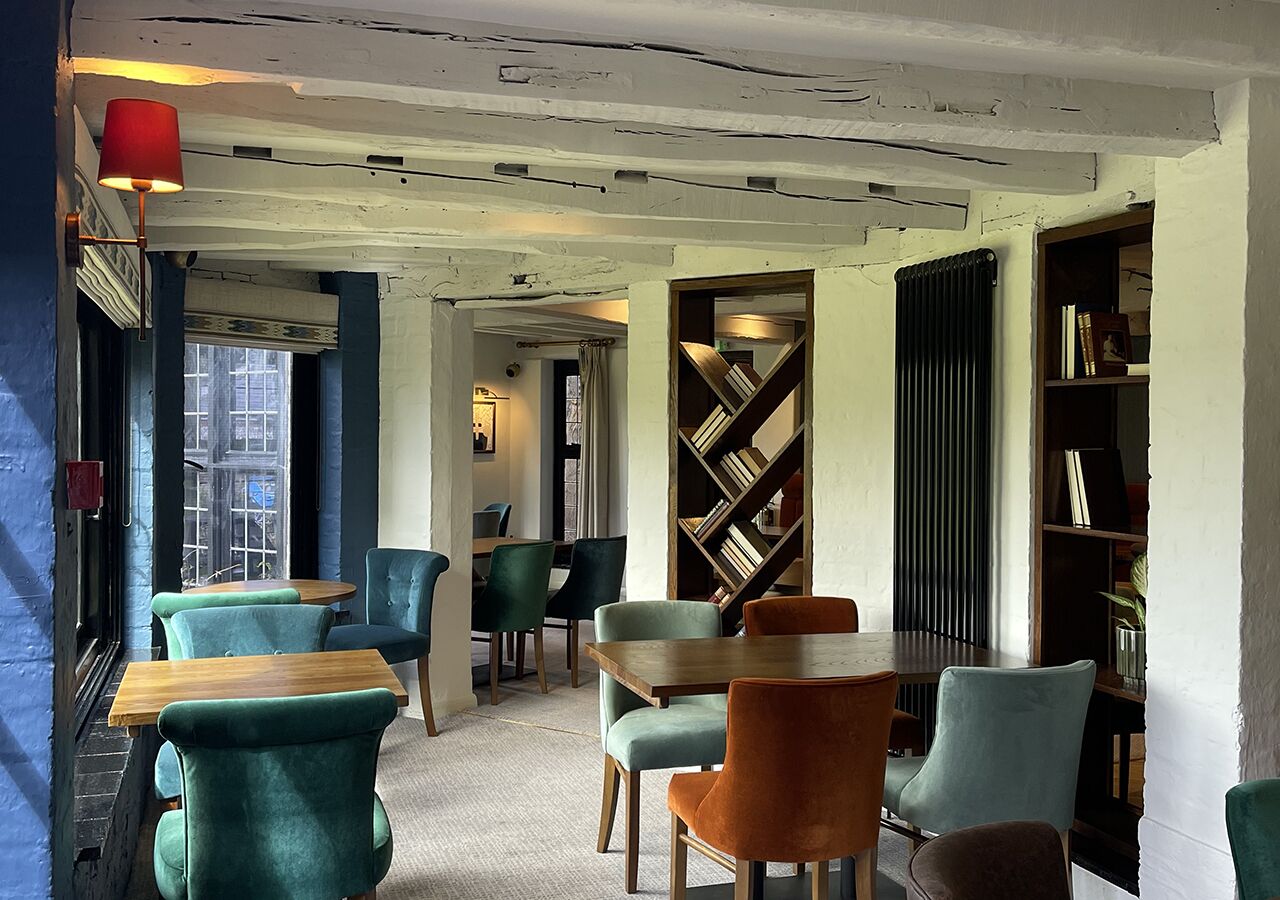 Un café acogedor con sillas color turquesa, mesas de madera y una estantería.