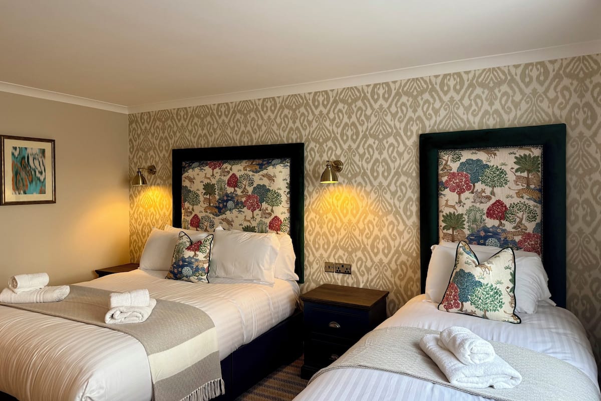 Habitación de hotel con dos camas, cada una con cabecera, mesitas de noche y lámparas.