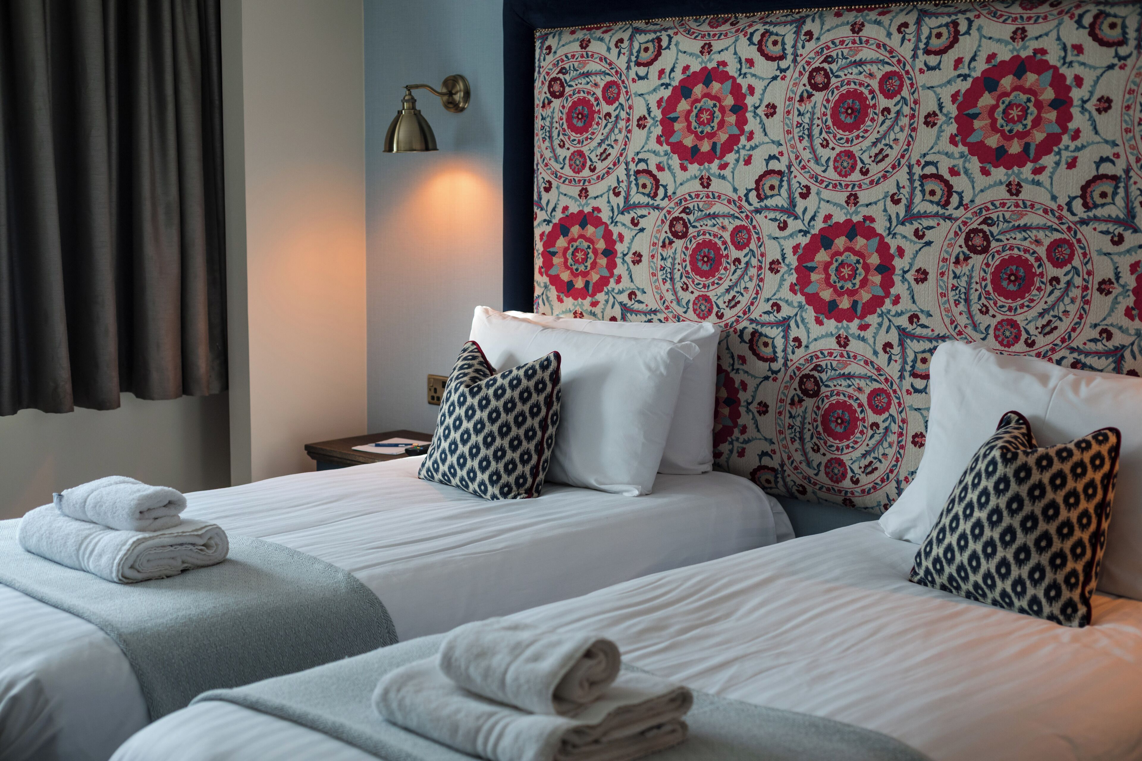 Een hotelkamer met twee bedden, een hoofdbord met een patroon en een nachtkastje met een lamp.