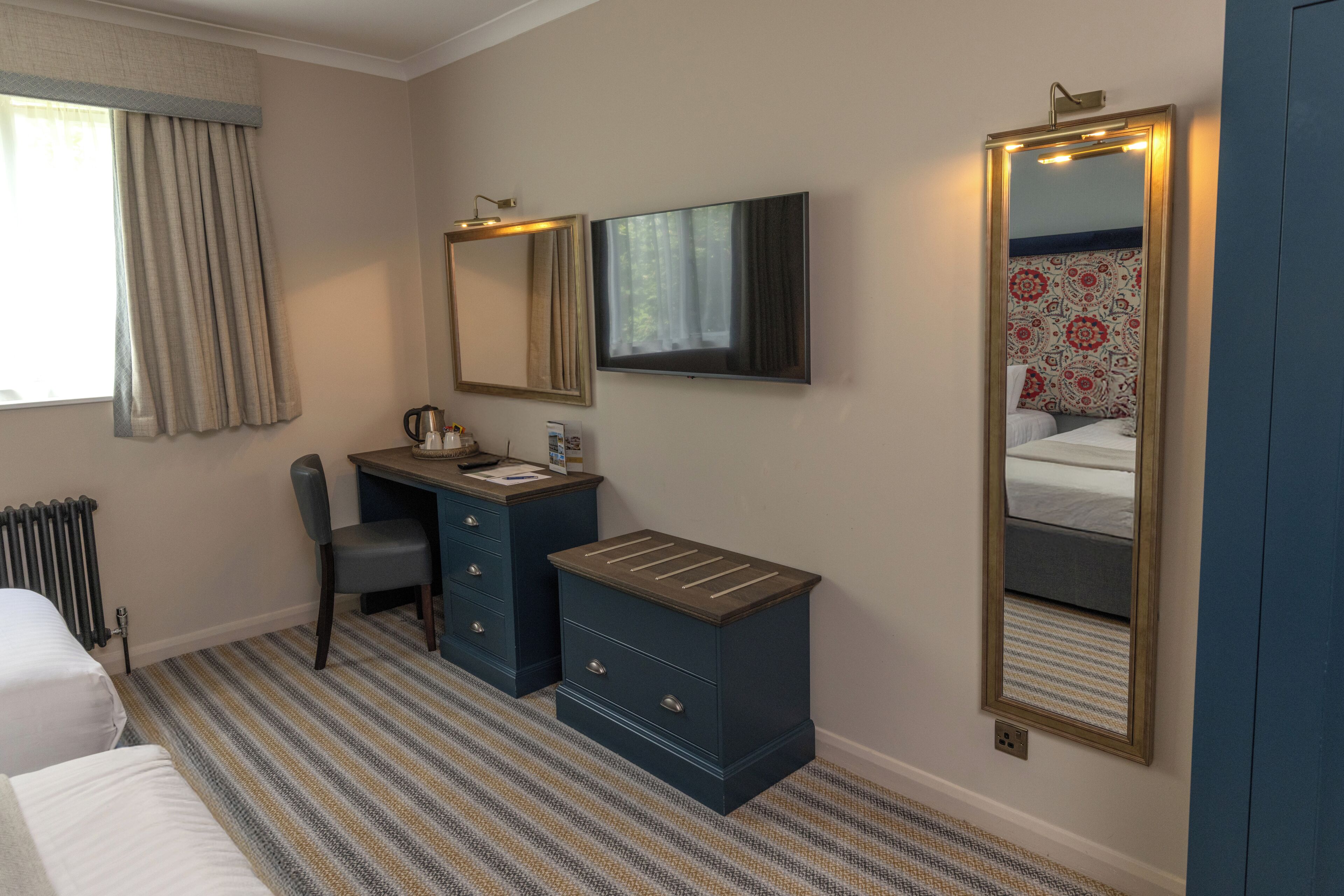 A hotel room with a bed, a desk with a chair, a large mirror, and a radiator.