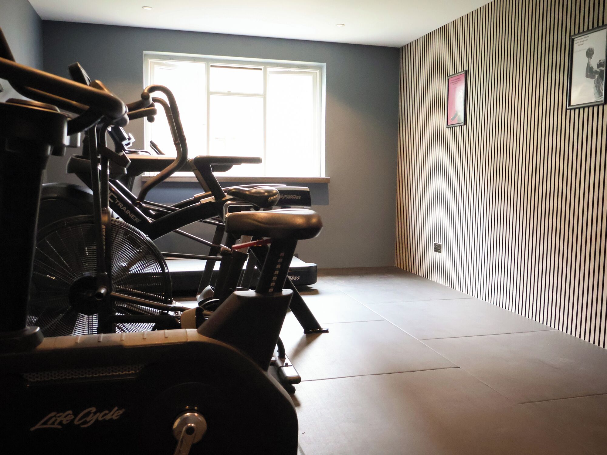 A room with a stationary bike, a window, and a striped wall.