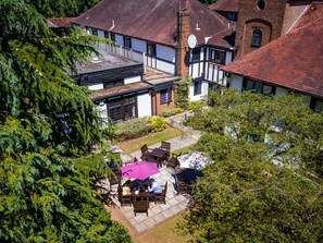 Un patio con zona de comedor, rodeado de edificios tradicionales con entramado de ladrillo y madera, y un árbol grande al frente.