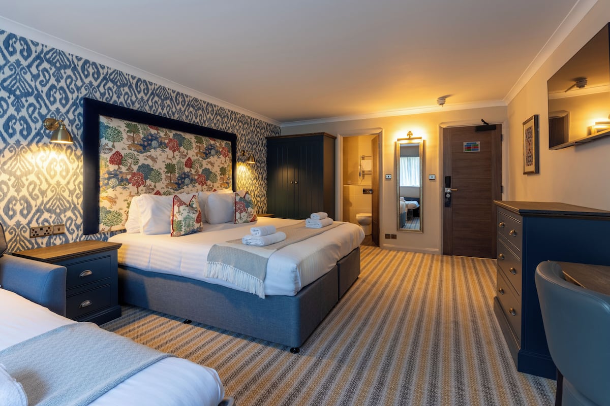 Una habitación de hotel con cama, mesitas de noche, armario, escritorio y espejo.