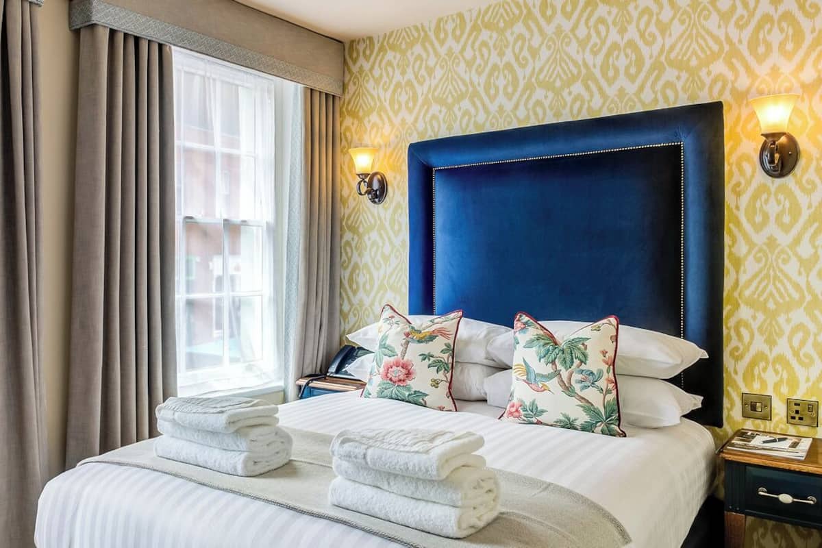 Una habitación de hotel con una cama grande, dos mesitas de noche, un ventanal con cortinas y papel tapiz estampado.
