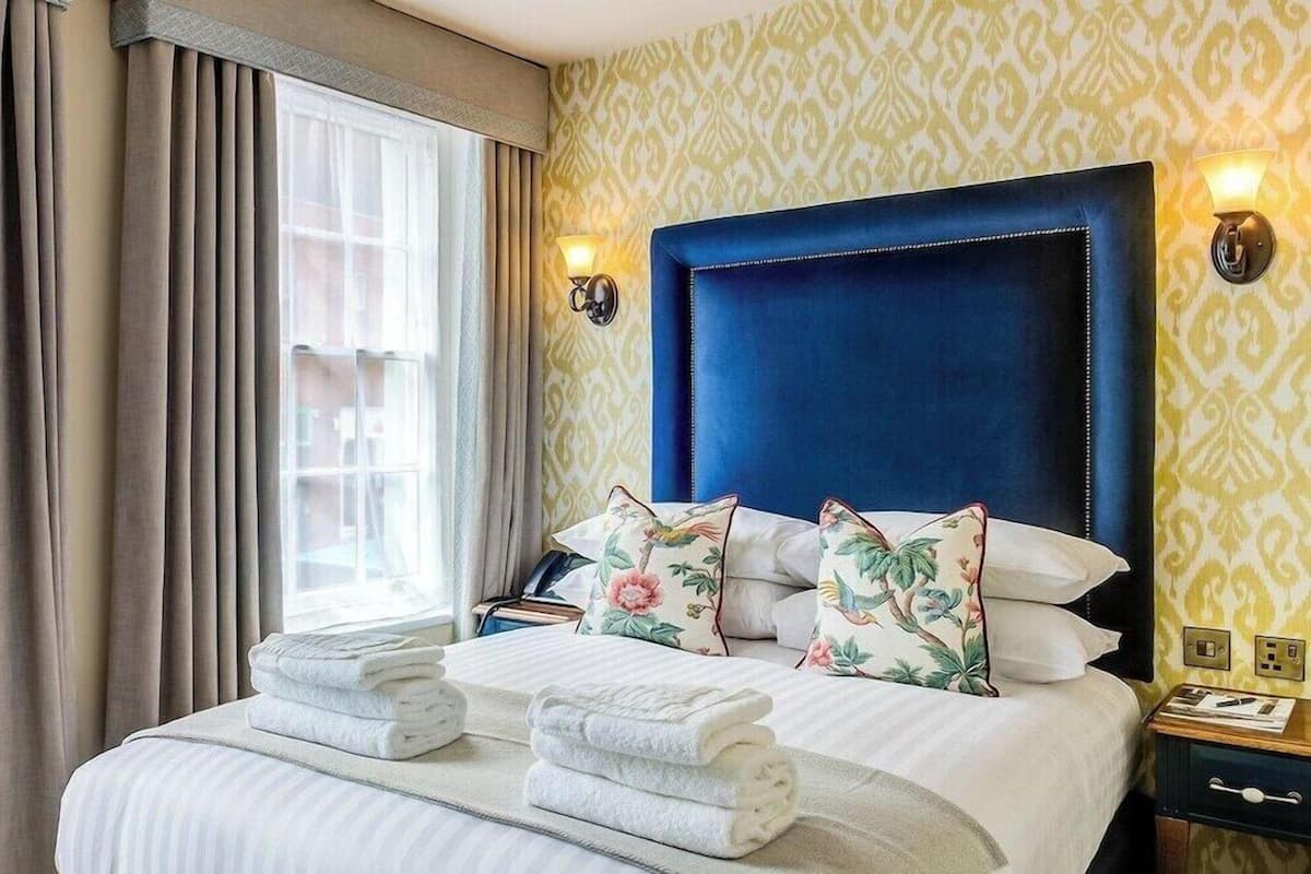 Una habitación de hotel con una cama grande, una mesita de noche, una lámpara y un ventanal con cortinas.