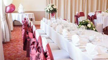 Une salle de banquet avec de longues tables dressées pour un événement formel, agrémentée de nappes blanches, de couverts en argent et de verres.