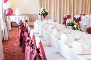 A banquet hall with long tables set for a formal event, featuring white tablecloths, silverware, and glassware.