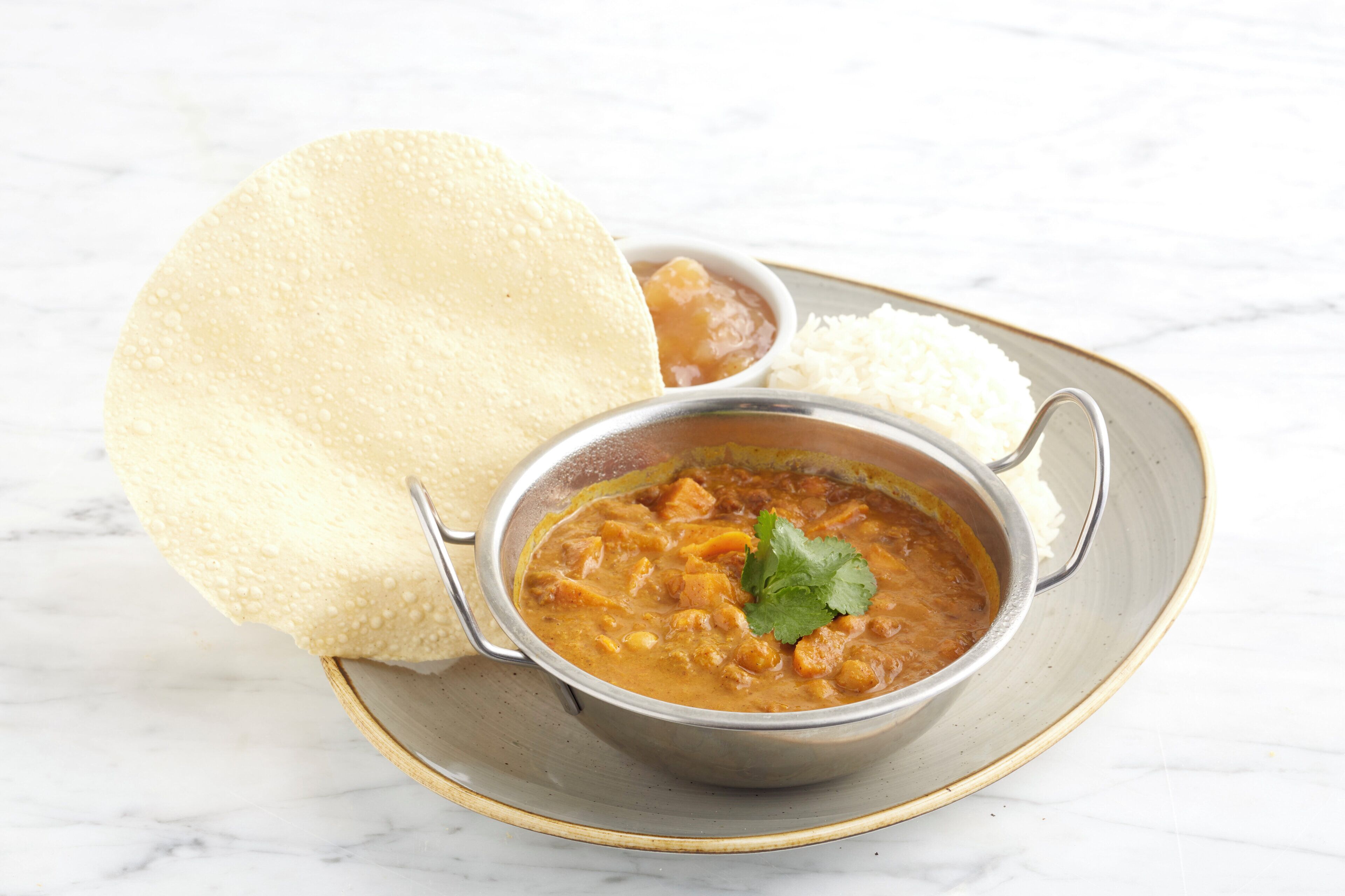 A bowl of curry with rice and a piece of naan bread on a plate.