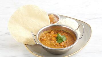 A bowl of curry with rice and a piece of naan bread on a plate.