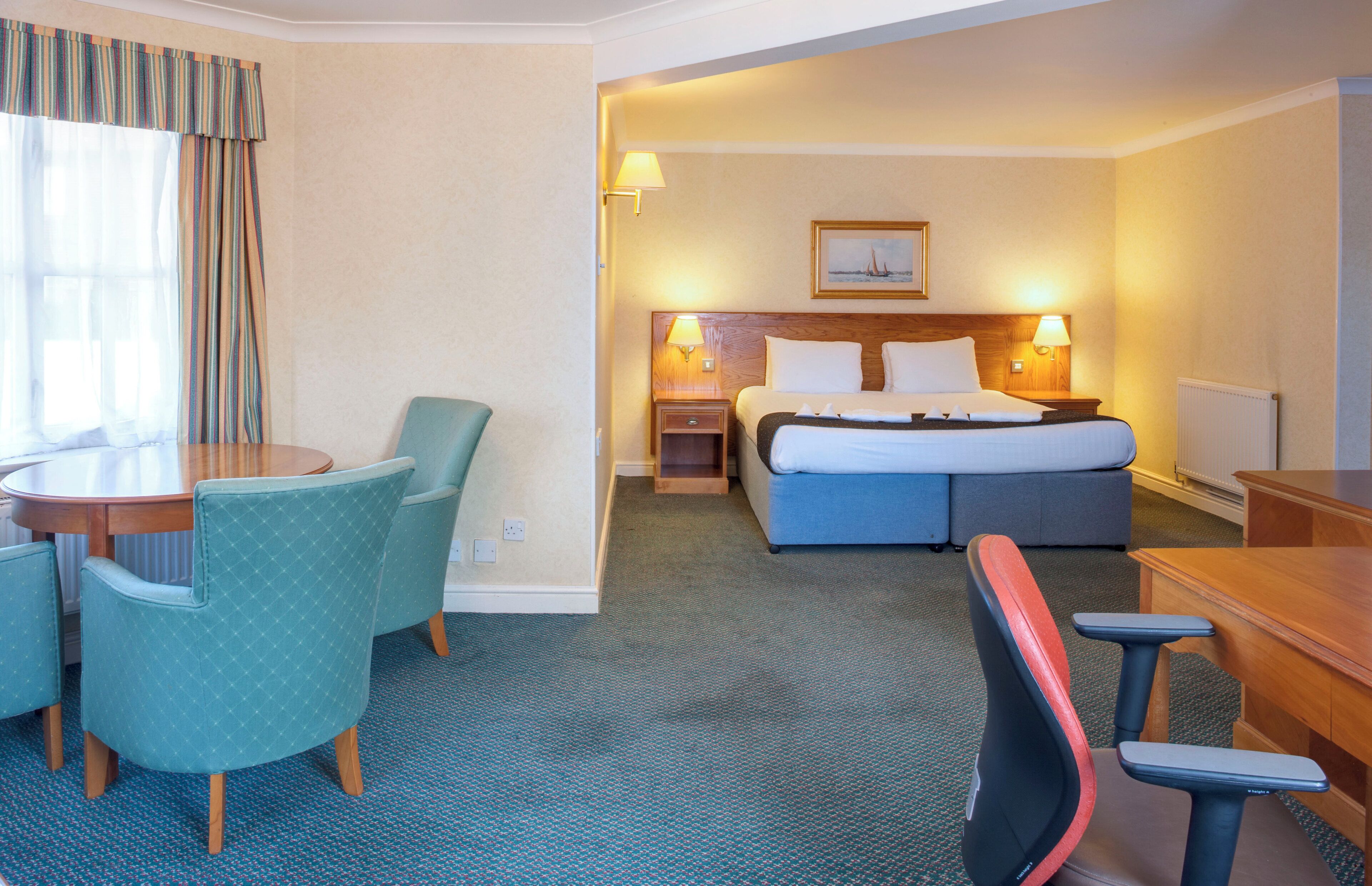 A hotel room with a bed, a desk, a chair, a table, and a window with curtains.