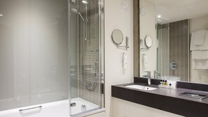A modern bathroom with a glass-enclosed shower, a white bathtub, a black countertop, and a large mirror. - Holiday Inn Ipswich Orwell by IHG (Ipswich)