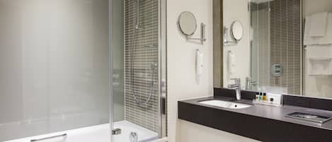 Un baño moderno con ducha envuelta en vidrio, una bañera blanca, encimera negra y un espejo grande.