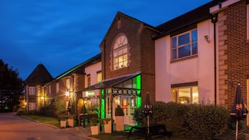 A hotel with a traditional brick facade, a covered outdoor seating area, and a well-lit entrance.