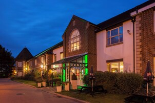 Un hotel con fachada de ladrillo tradicional, un área de estar exterior cubierta y una entrada bien iluminada.
