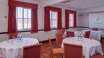 A conference room with round tables, chairs, and red curtains.