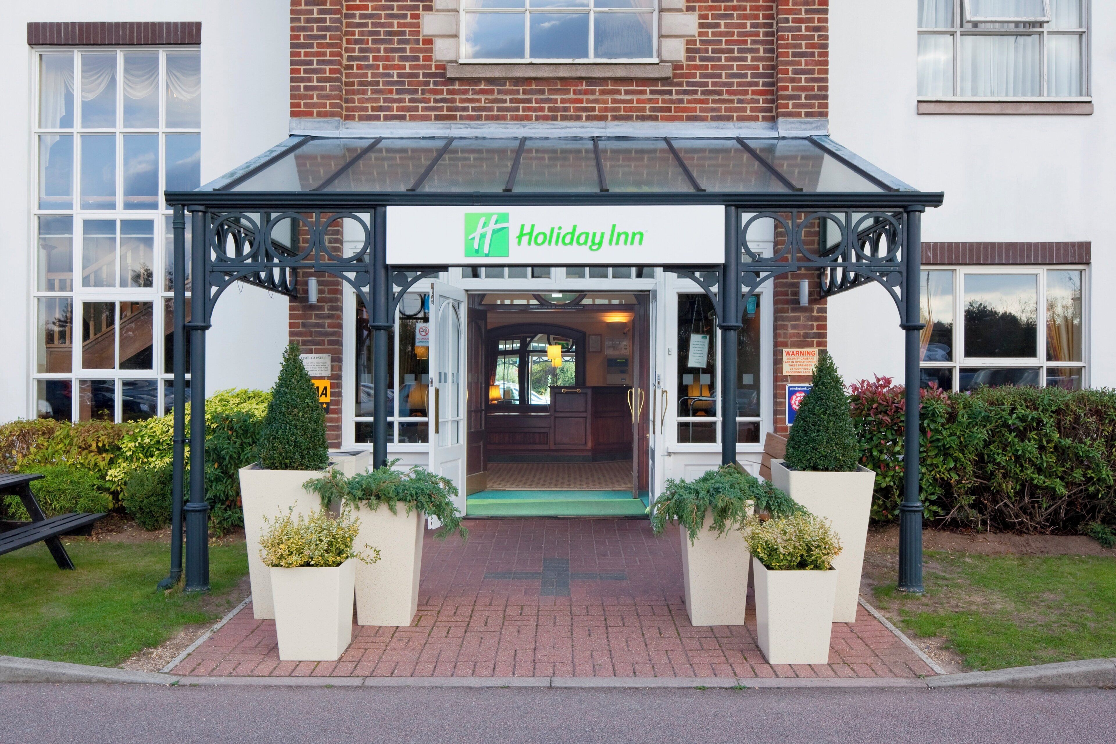 A Holiday Inn entrance with a covered walkway, brick facade, and potted plants.