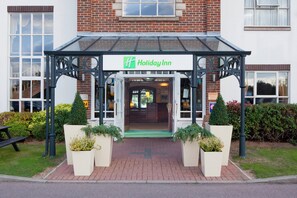A Holiday Inn entrance with a covered walkway, brick facade, and potted plants. - Holiday Inn Ipswich Orwell by IHG (Ipswich)