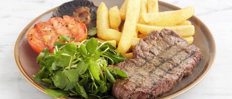 A plate with steak, fries, a slice of tomato, and greens.