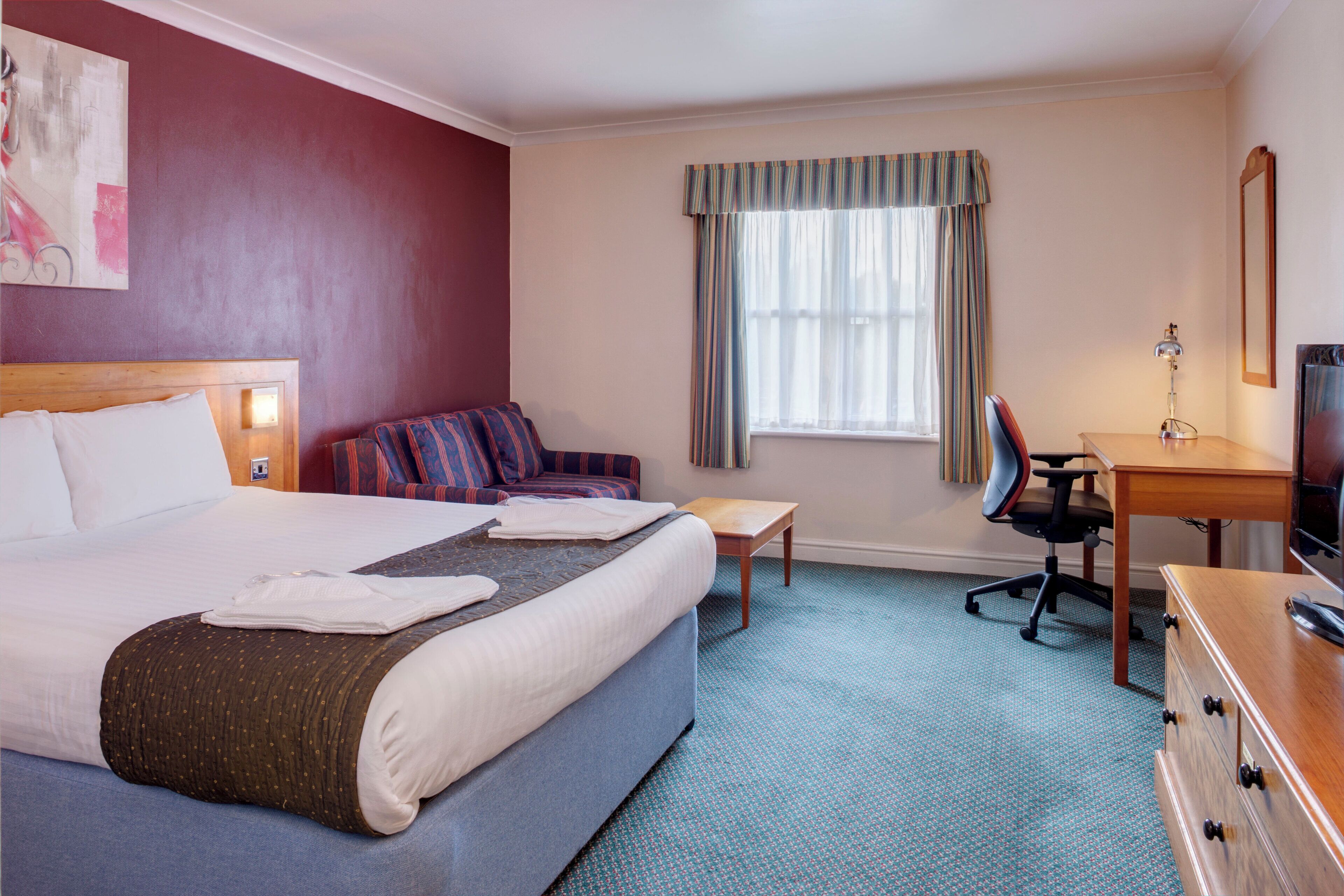 A hotel room with a bed, a desk, a chair, a television, and a window with curtains.