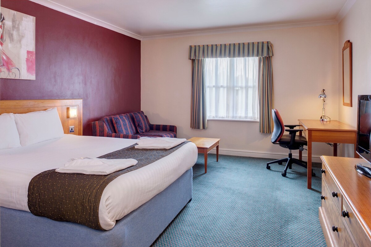 A hotel room with a bed, a desk, a chair, a television, and a window with curtains.