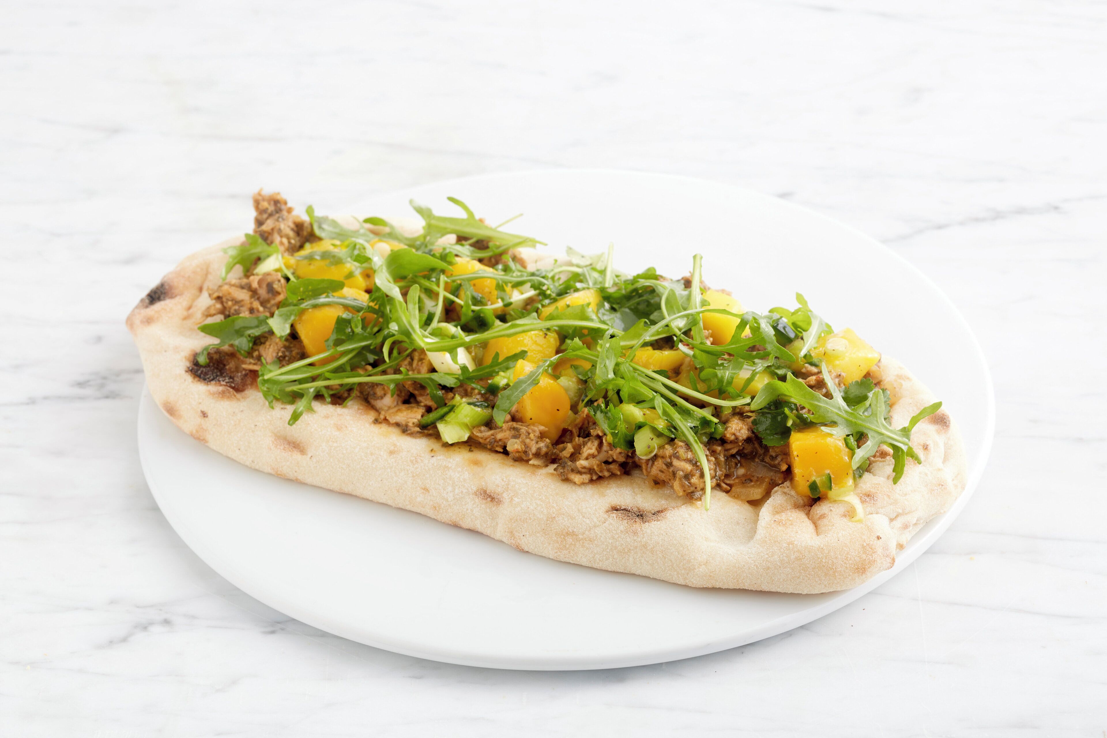 A flatbread topped with meat and vegetables on a white plate.