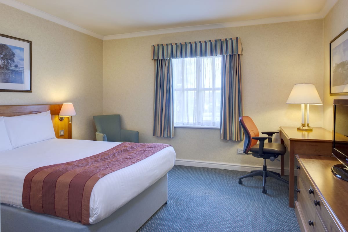 A hotel room with a large bed, a desk, a chair, and a window with curtains.
