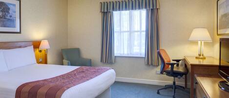 A hotel room with a large bed, a desk, a chair, and a window with curtains.