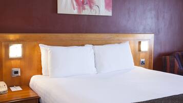 Habitación de hotel con cabecera de madera, ropa de cama blanca, mesita de noche con teléfono y lámpara de pared.