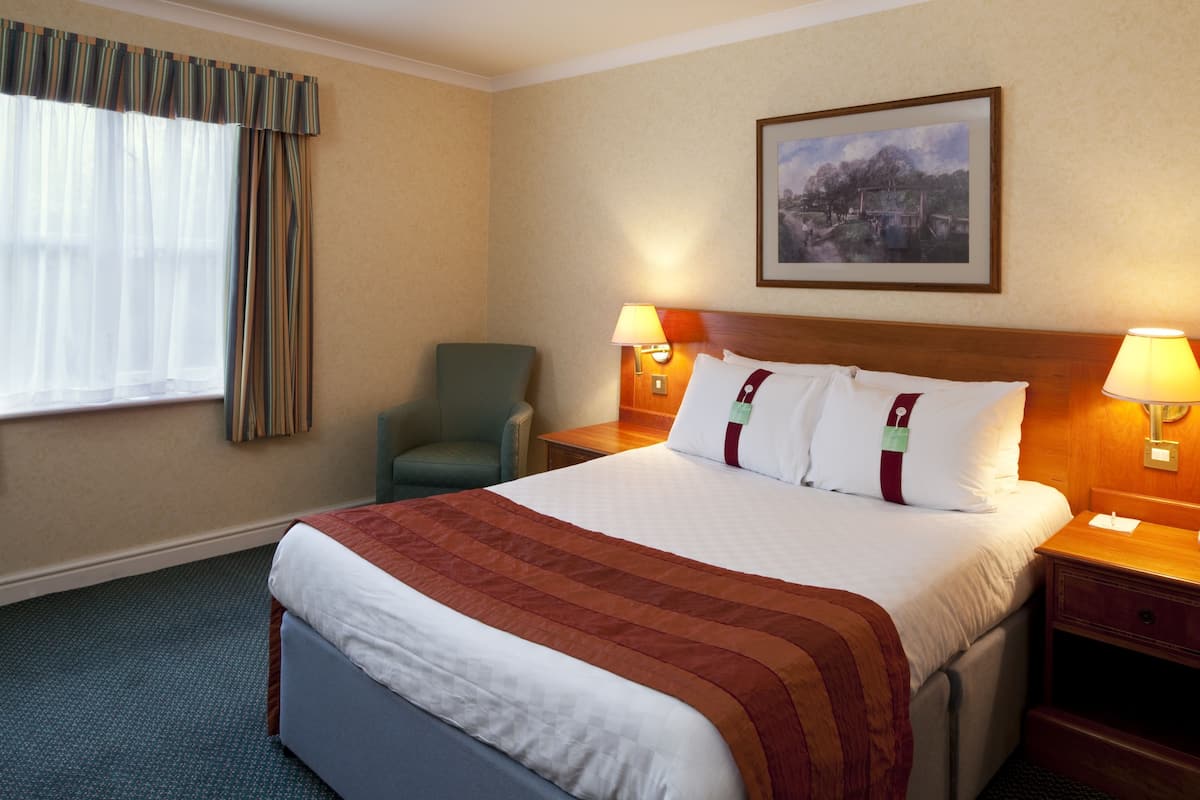 A hotel room with a large bed, two bedside lamps, a chair, a nightstand, and a painting on the wall.