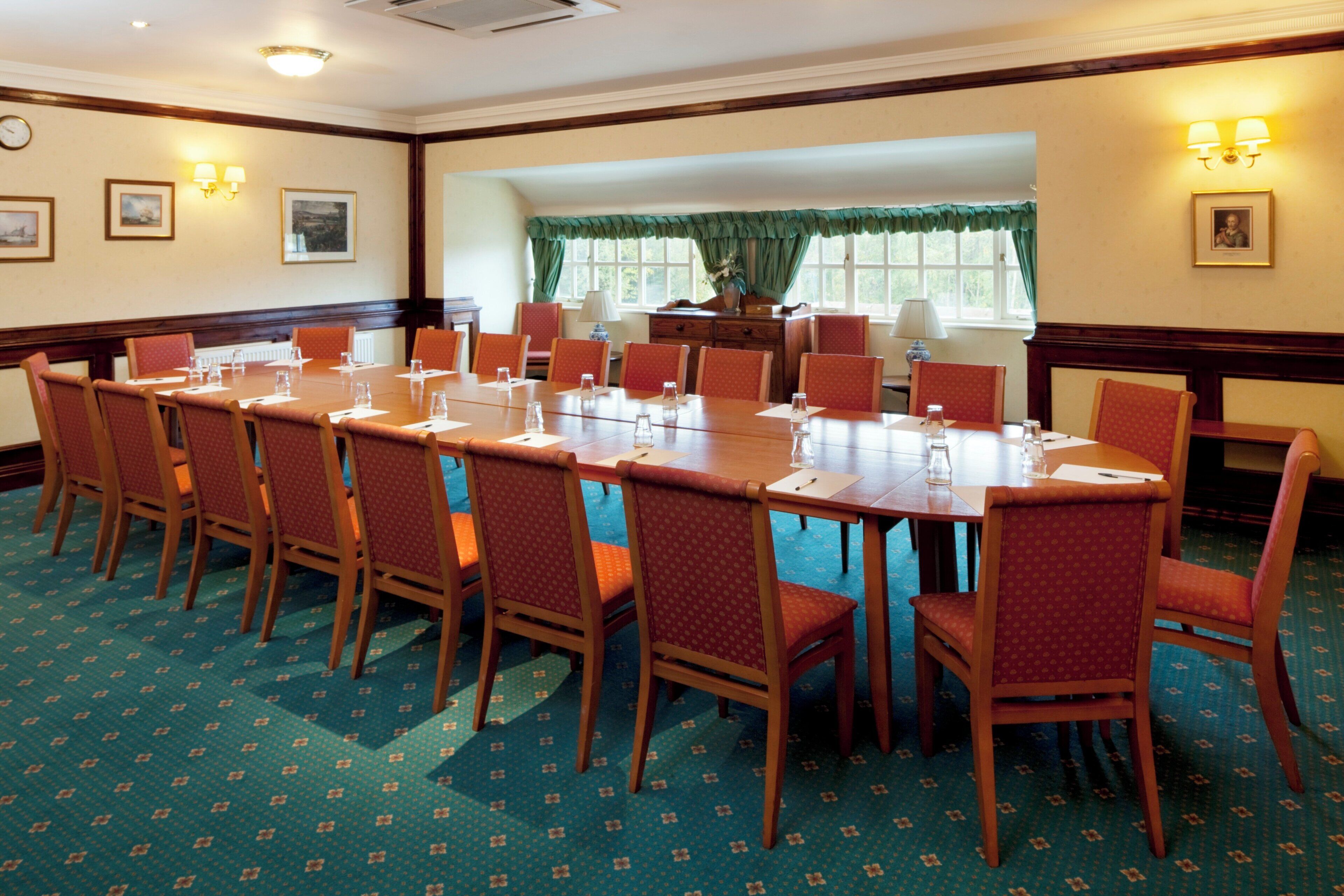 A conference room with a long table, multiple chairs, and a window with curtains.