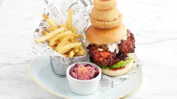 Un pasto composto da un hamburger con una polpetta fritta, porzione di patatine fritte e una piccola ciotola di insalata di cavolo.