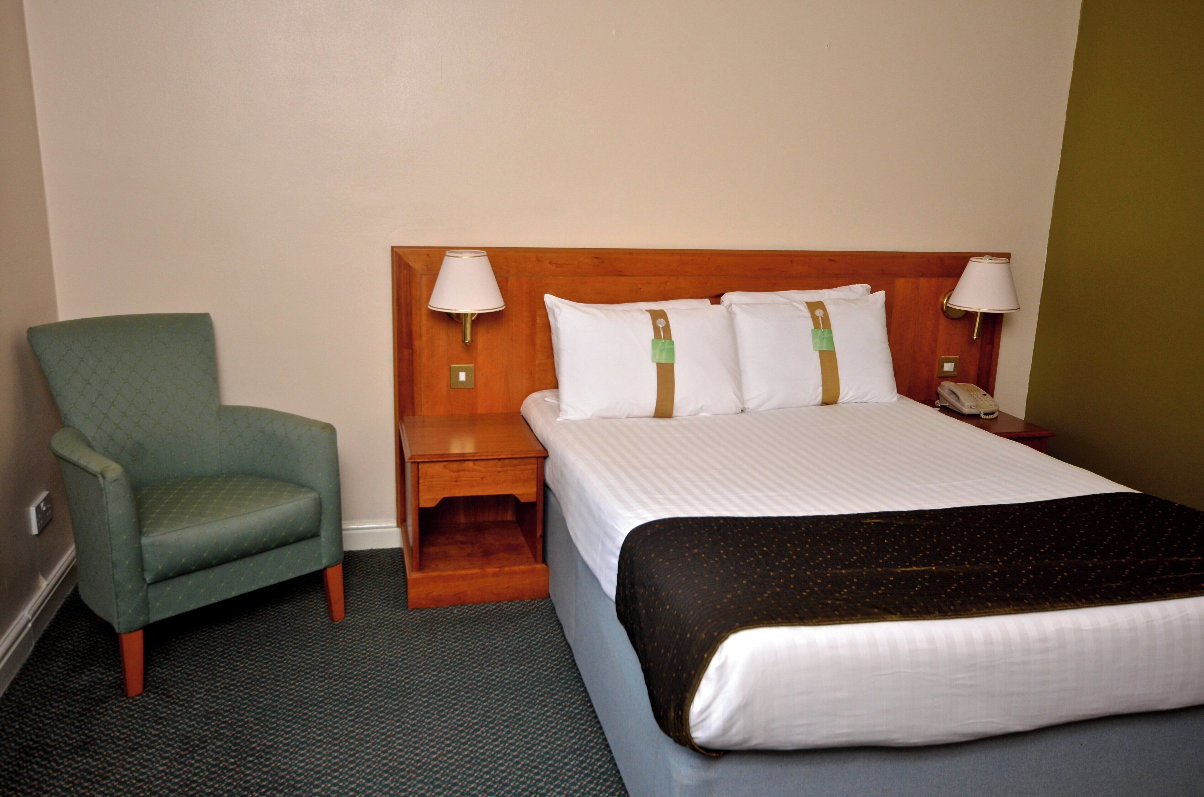 A hotel room with a single bed, a bedside table with a lamp, a chair, and a telephone.