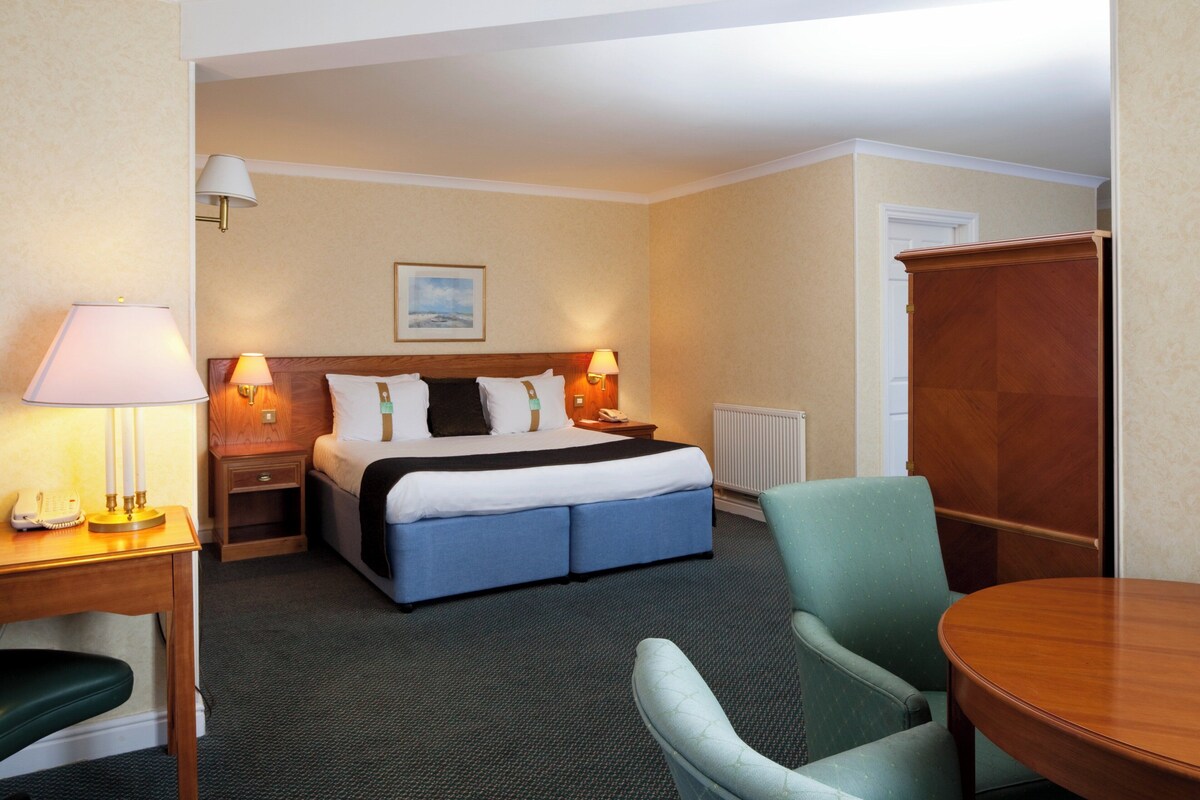 A hotel room with a bed, bedside lamps, a desk with a telephone, a chair, and a table.