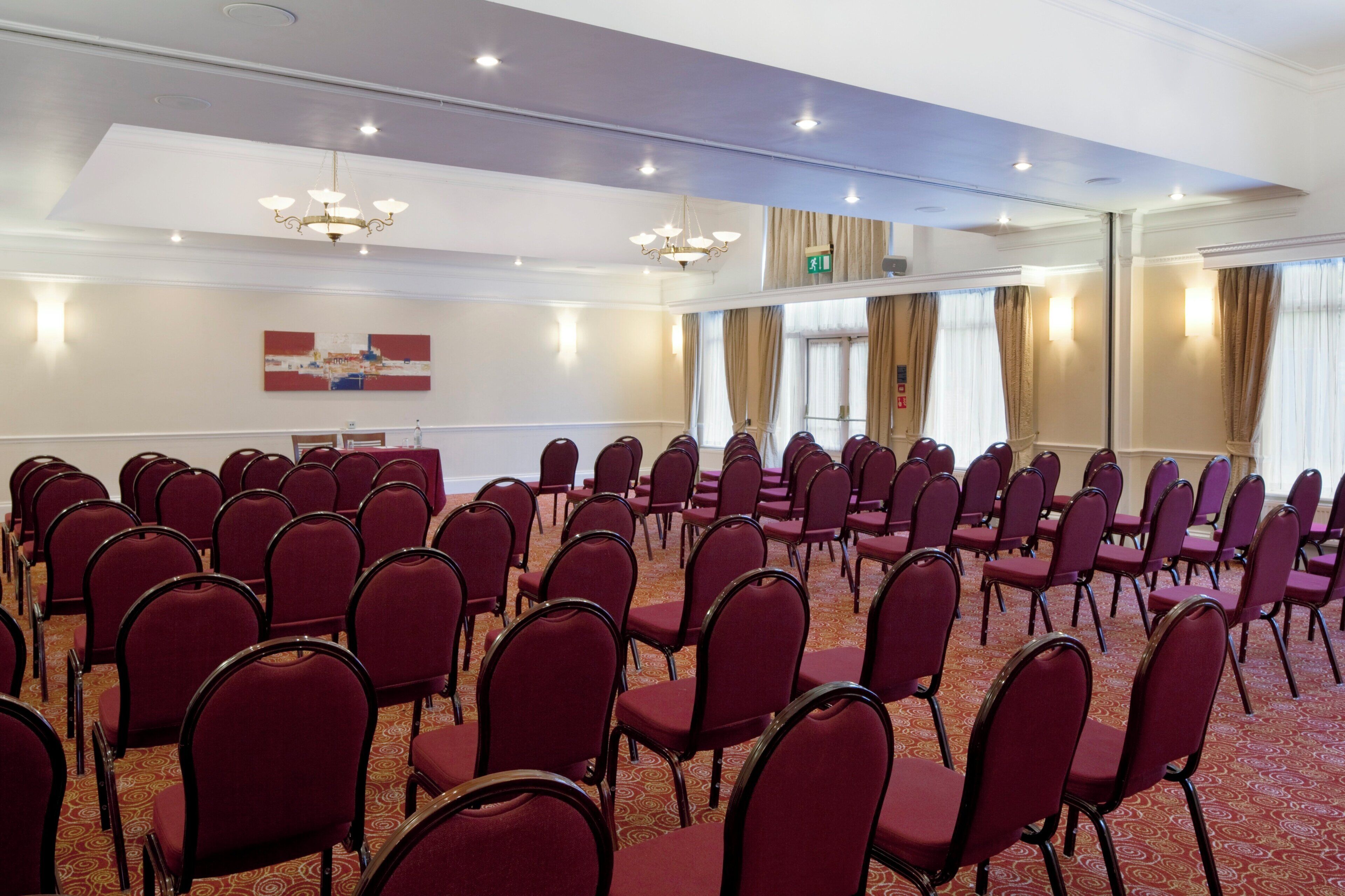 A conference room with rows of red chairs, a carpeted floor, and a chandelier.