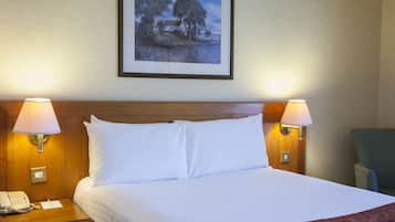 Hotelkamer met groot bed, twee bedlampen, een ingelijst schilderij aan de muur, een houten hoofdbord, een nachtkastje met telefoon en notitieboekje, en een groene stoel.