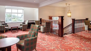 A spacious room with a patterned carpet, multiple chairs, a table, and a staircase with a railing. - Holiday Inn Ipswich Orwell by IHG (Ipswich)