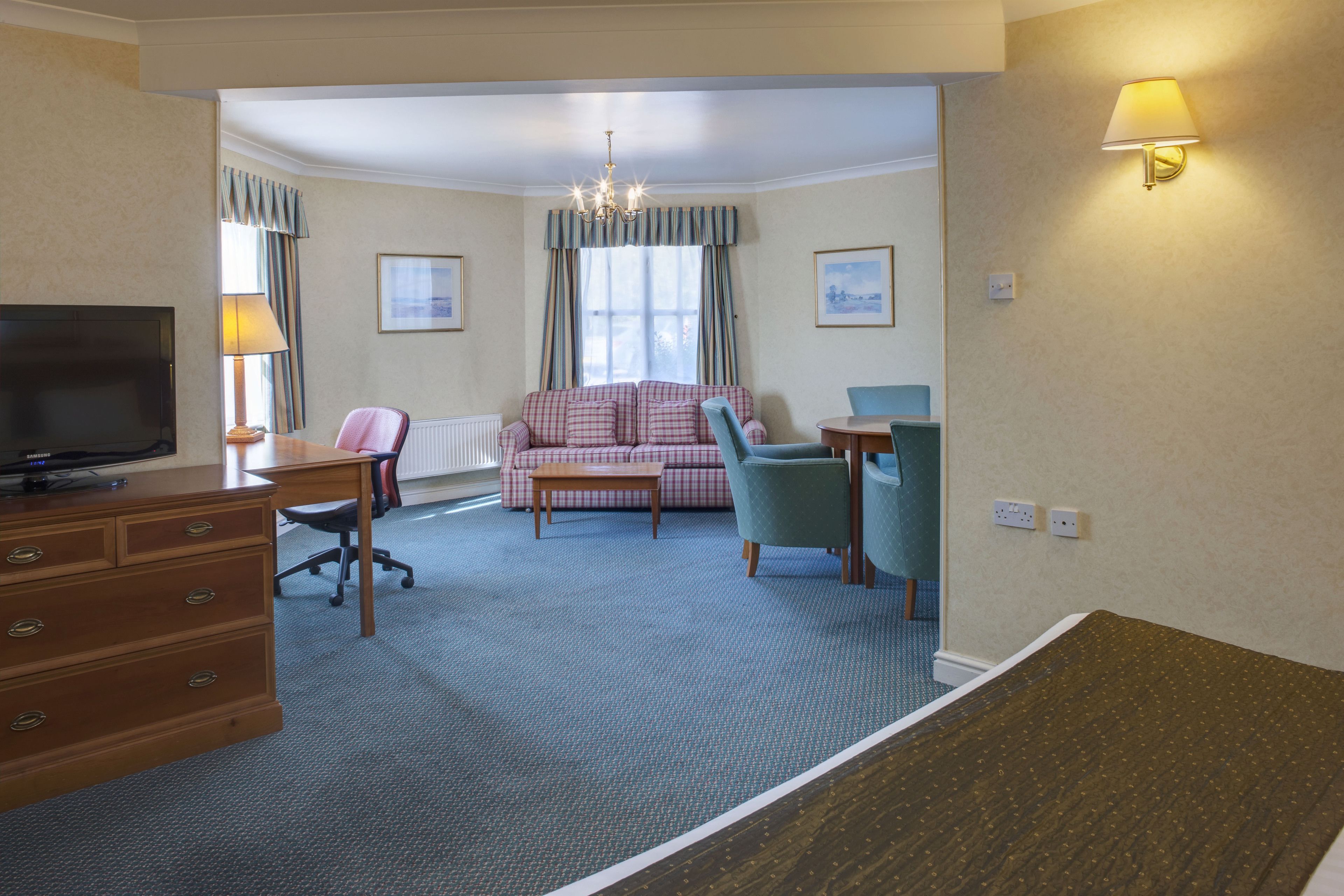 A hotel room with a television, a desk, a sofa, and a chair.