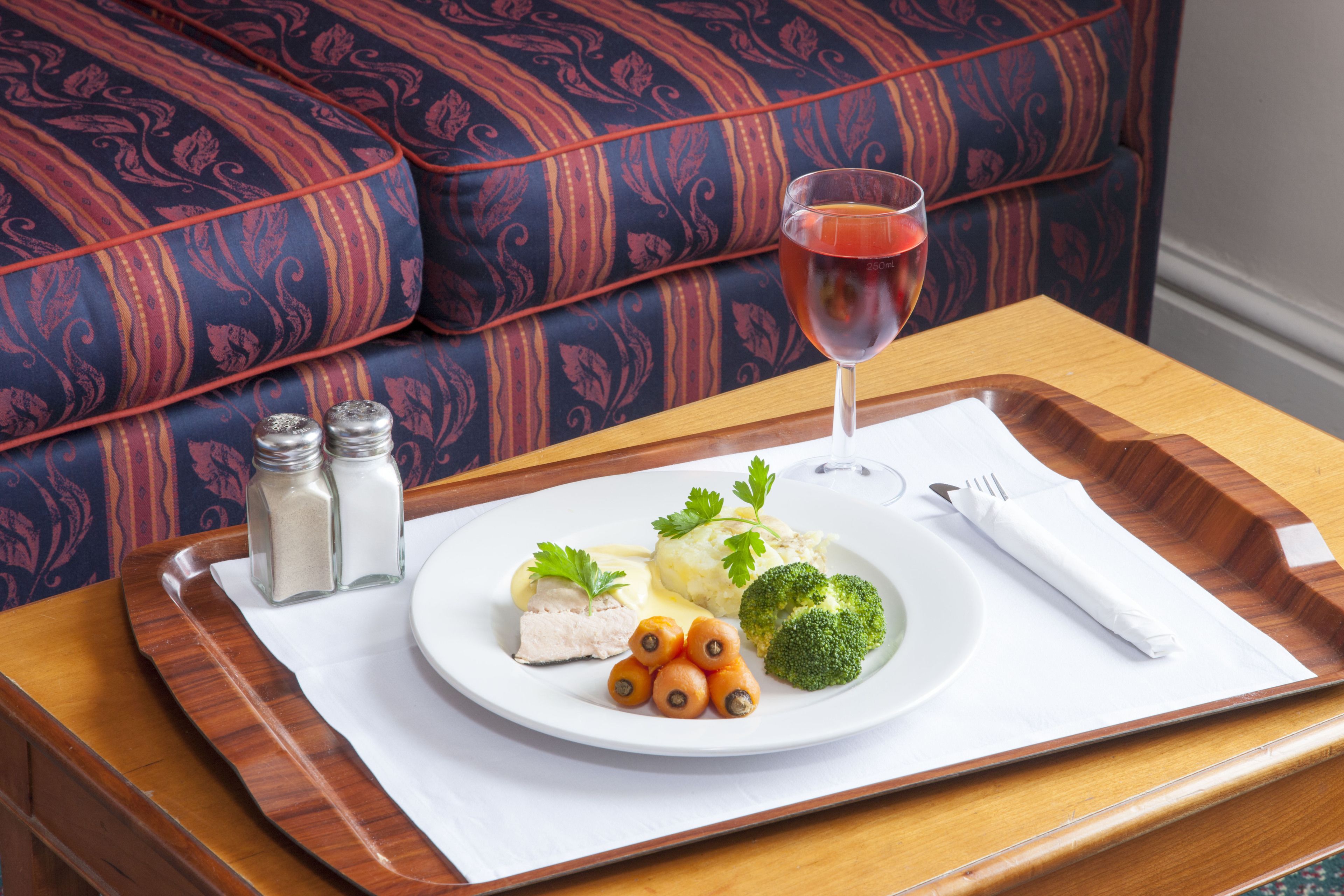 A dining table with a plate of food, a glass of red drink, and a napkin.