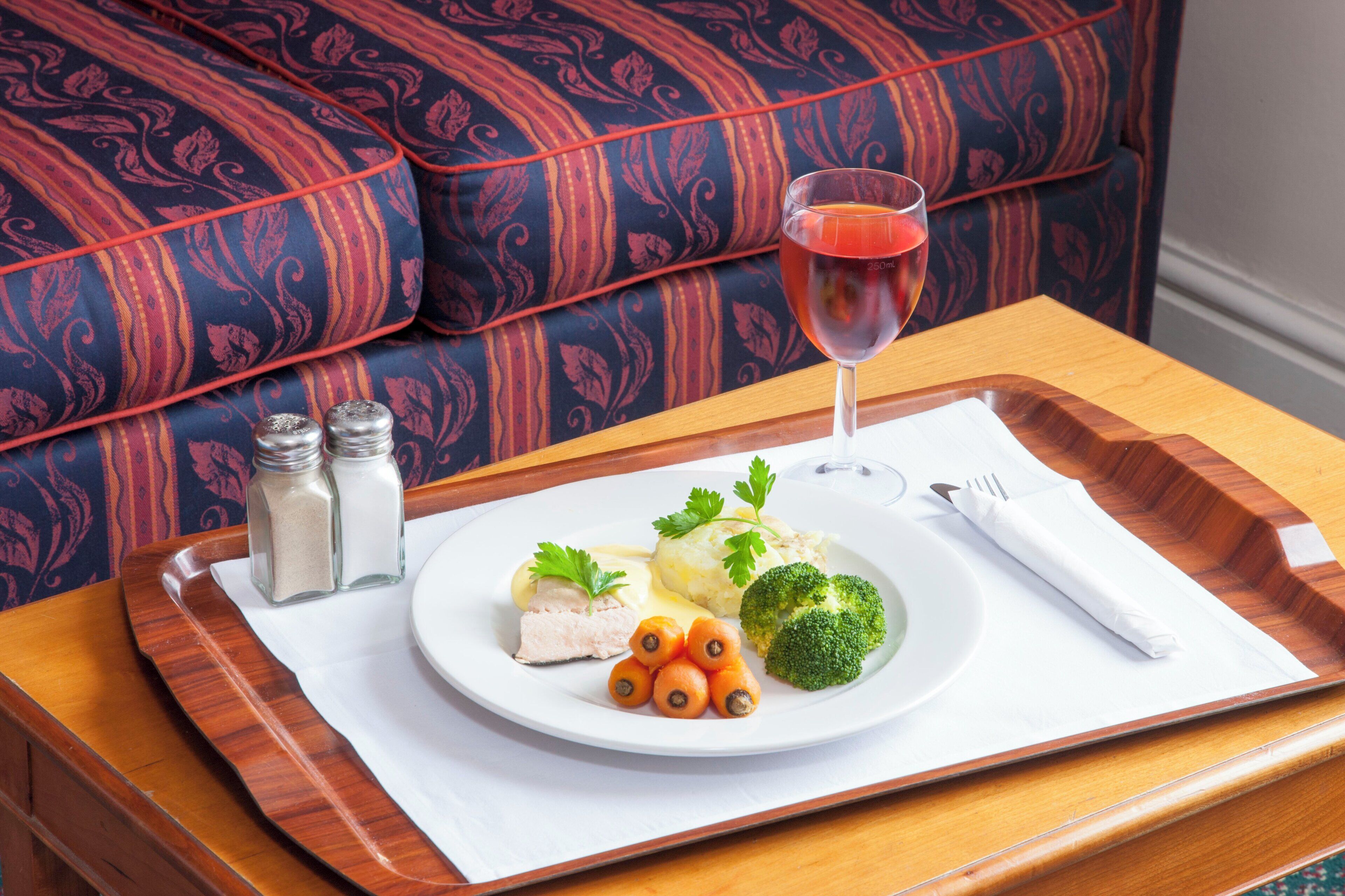 A dining setup with a plate of food, a glass of red beverage, and a napkin on a tray.