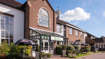A Holiday Inn with a traditional brick facade, a covered outdoor seating area, and a clear blue sky.