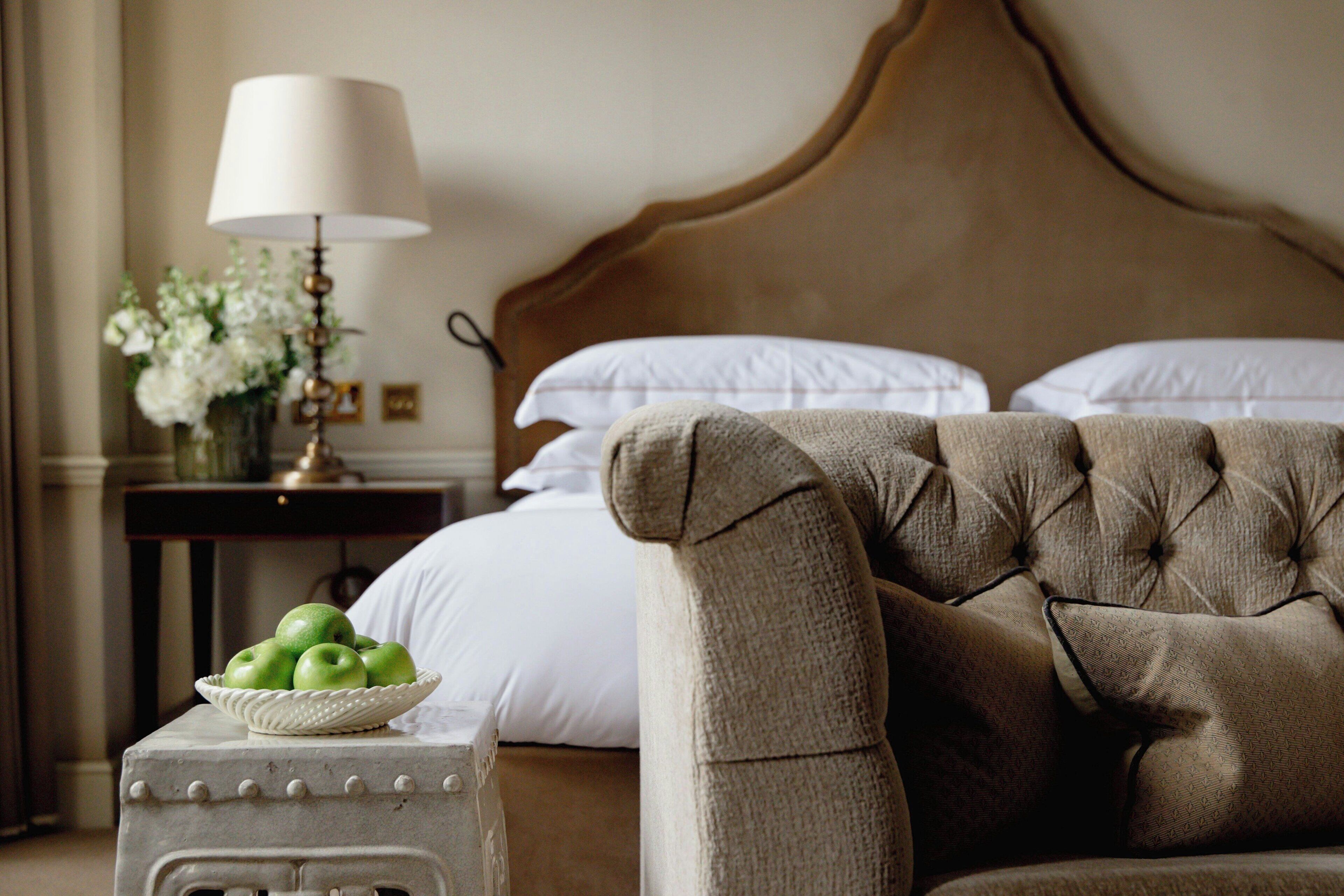 A bedroom with a tufted headboard, a bedside table with a lamp, and a bowl of green apples.