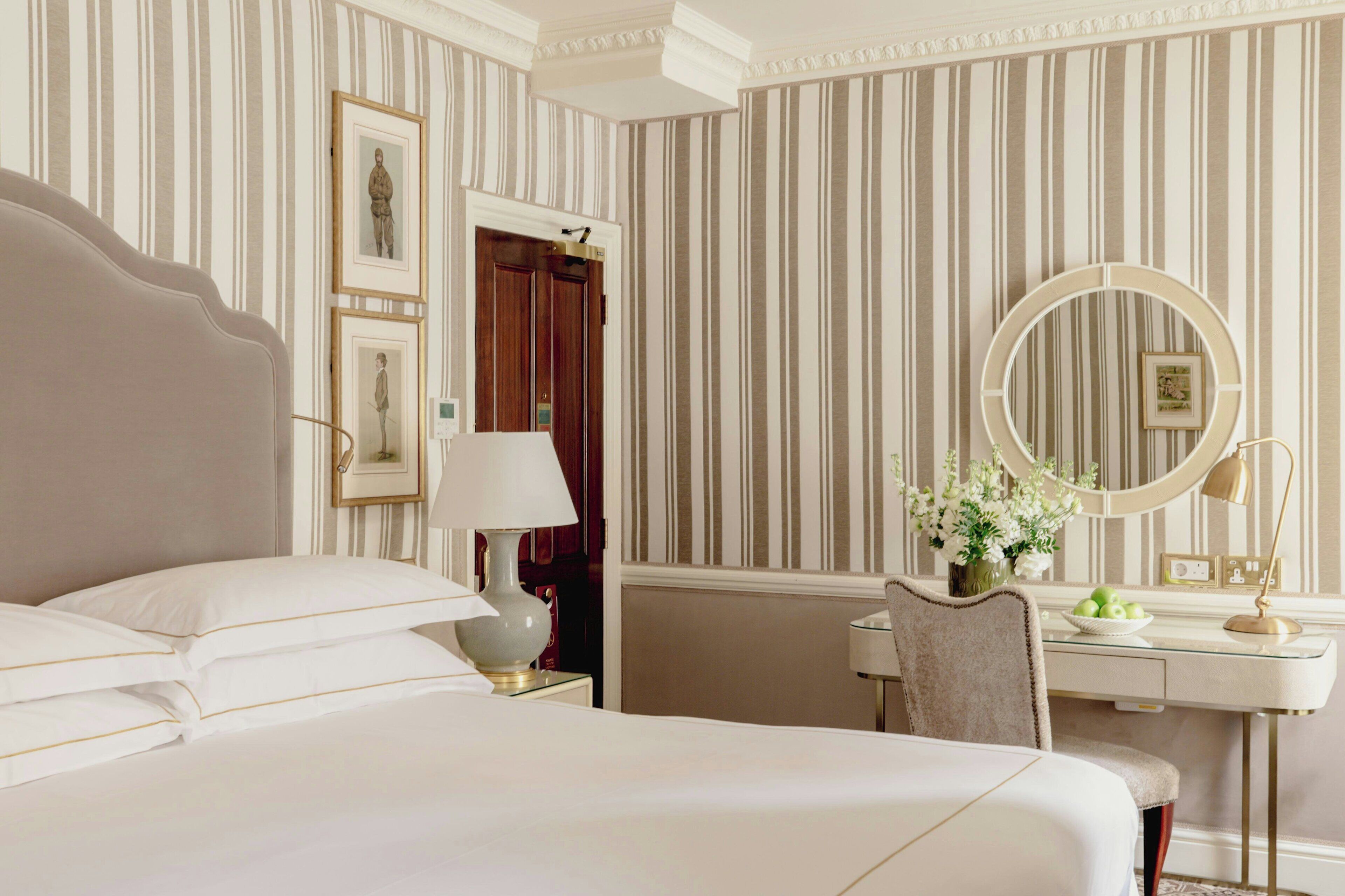 Une chambre d’hôtel avec un grand lit, un bureau avec une chaise, un miroir rond et une commode.