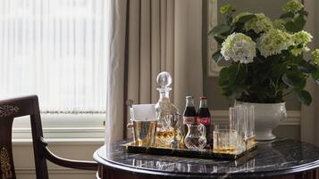 A table with a tray holding a decanter, glasses, and bottles, a potted plant with white flowers, and a chair.