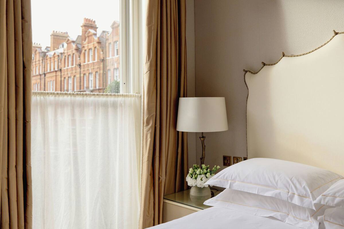 A hotel room with a bed, a bedside table with a lamp, and a window with curtains.