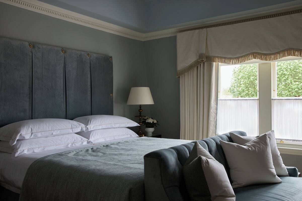 A bedroom with a large bed, a nightstand with a lamp, and a window with curtains.